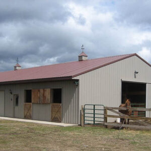 stable for horses. Tan building with a red roof and fenced in area for horses